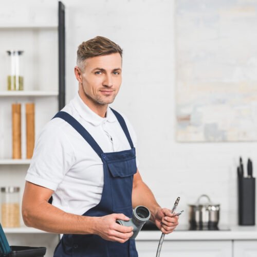 adult repairman holding pipes for kitchen faucet repairing and looking at camera